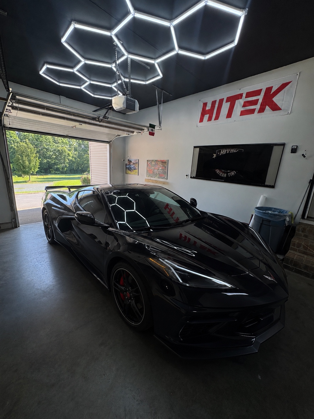 Black Corvette in the JTS home garage under hexagonal shop lights